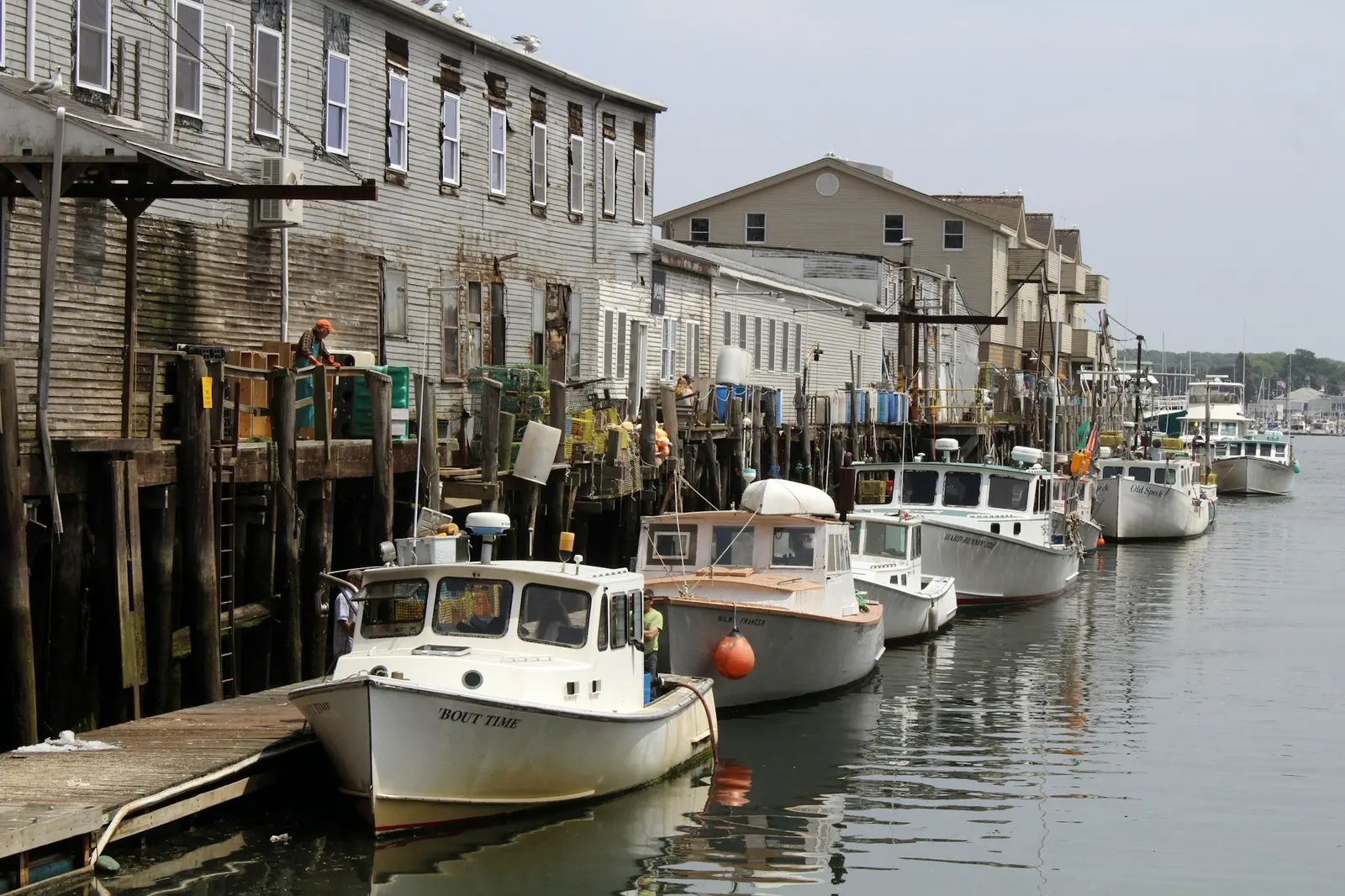 A white boat tied up at a wooden dock by a harbour building
