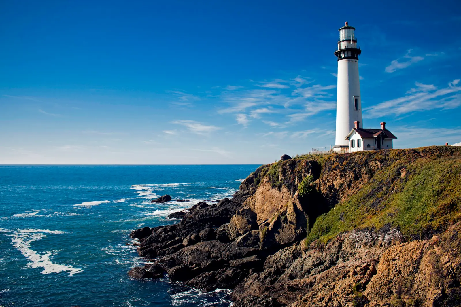 A white lighthouse on the coast under a cloudy sky